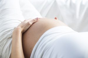 Schwangere Frau hält Hände schützend um Bauch,